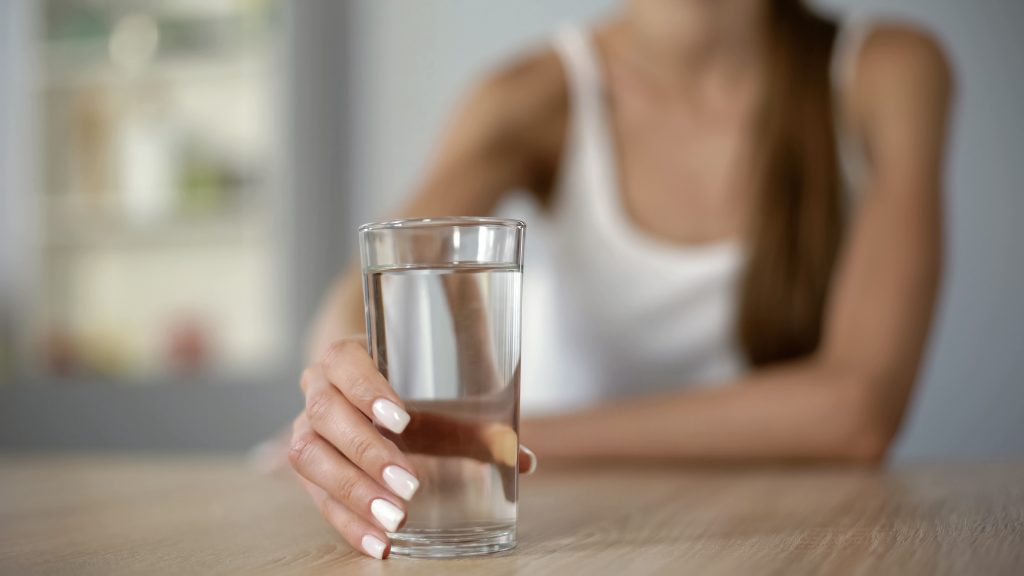 Persoon drinkt een glas water als onderdeel van een gezonde ochtendroutine.