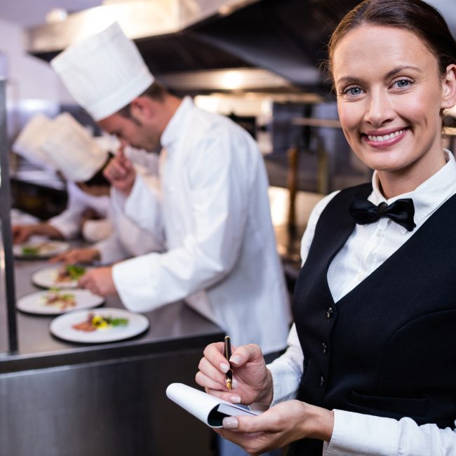 Lachende serveerster met notitieblok in een professionele keuken