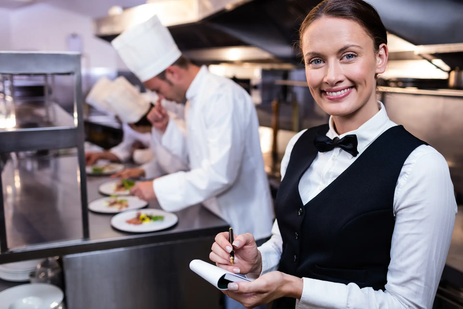 Lachende serveerster met notitieblok in een professionele keuken
