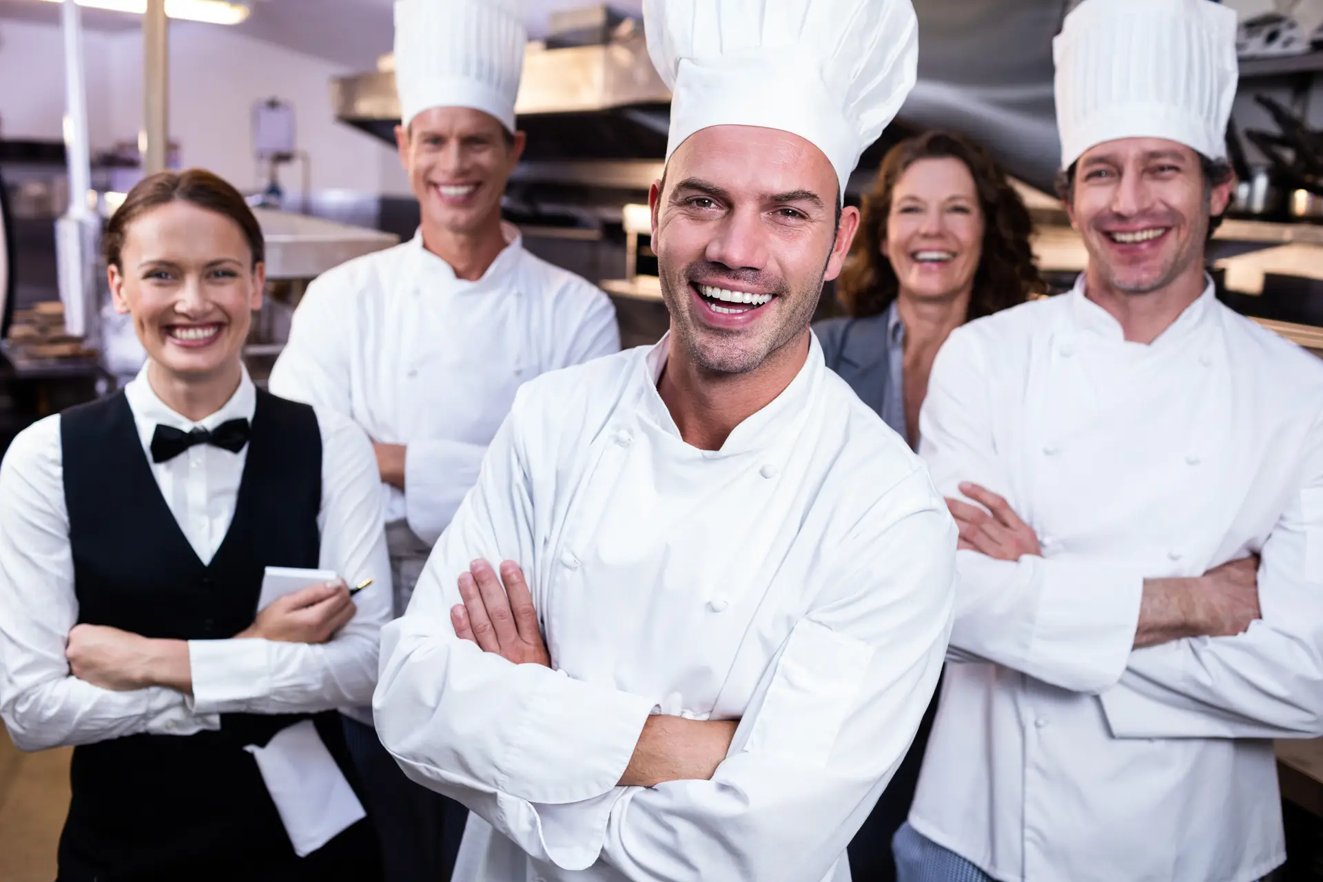Portret van een blij restaurantteam dat samen met gekruiste armen in een commerciële keuken staat