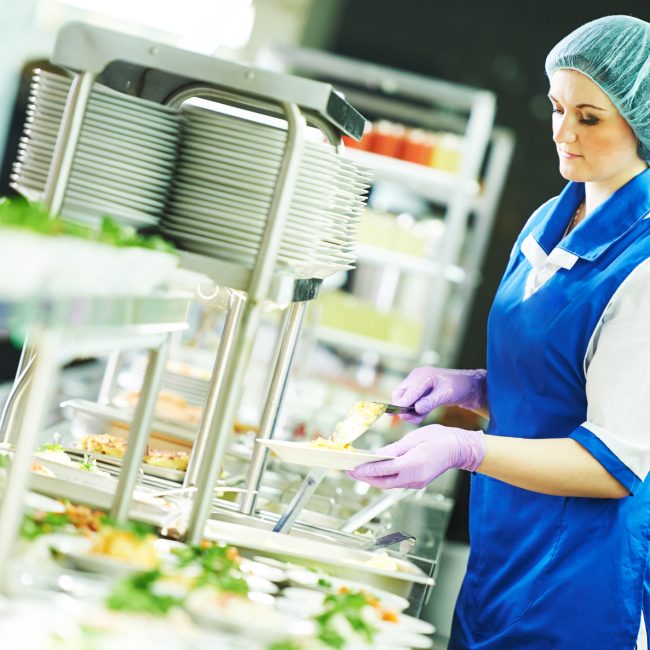 Buffet female worker servicing food in cafeteria.