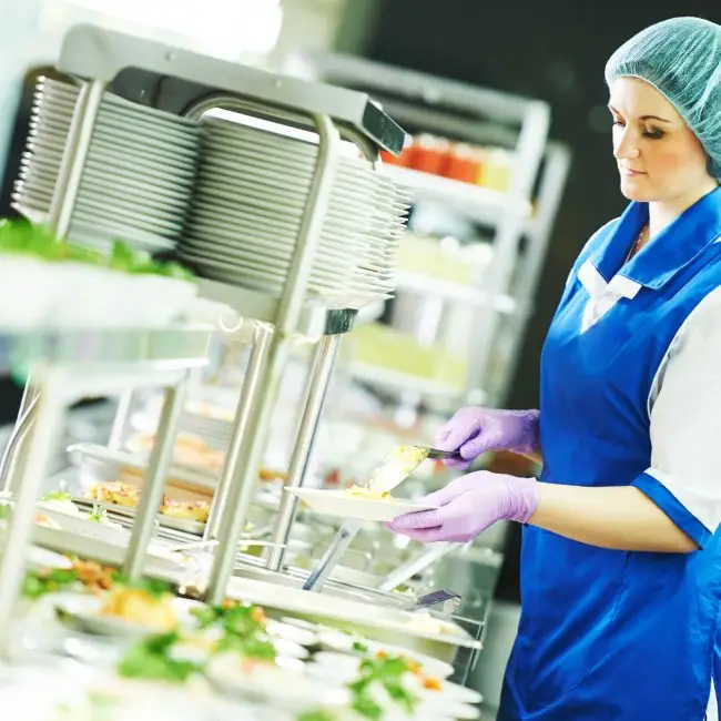 Buffet female worker servicing food in cafeteria.