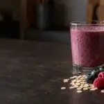 Glas smoothie naast bessen, havermout, walnoten en kruiden, als voorbeeld van ingrediënten die je in één drank kunt combineren.